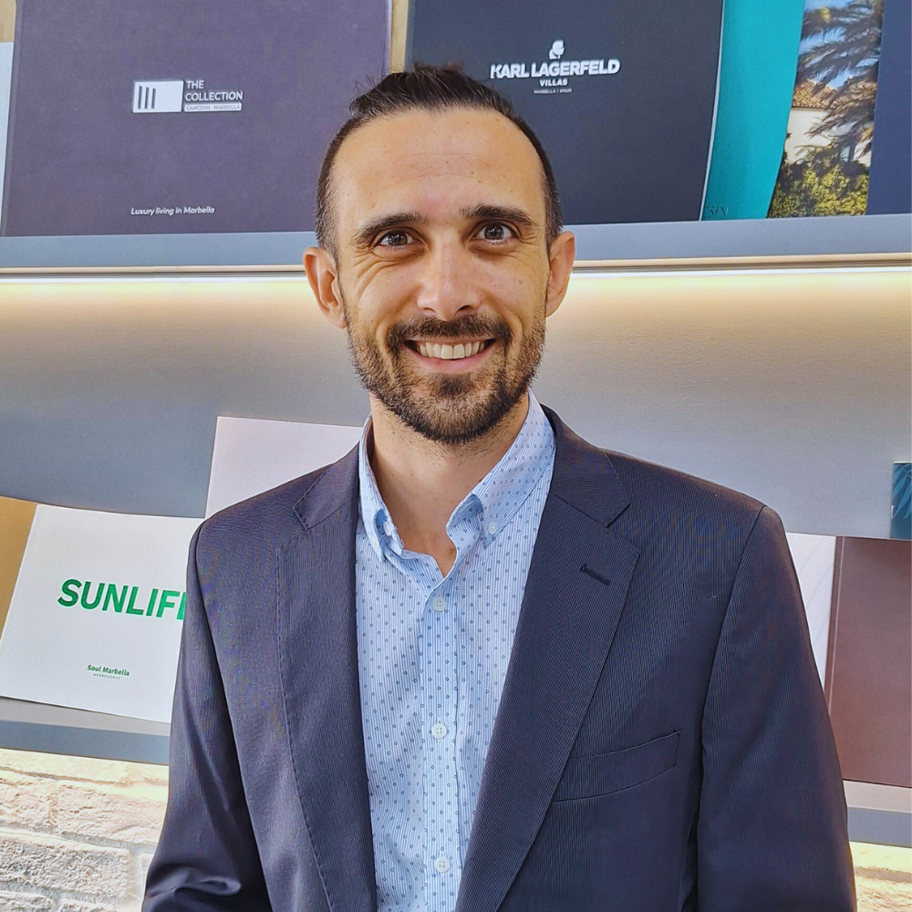 Izidor Isakov, a realtor from Spain, stands in a suit in front of brochures advertising new developments on the Costa del Sol.