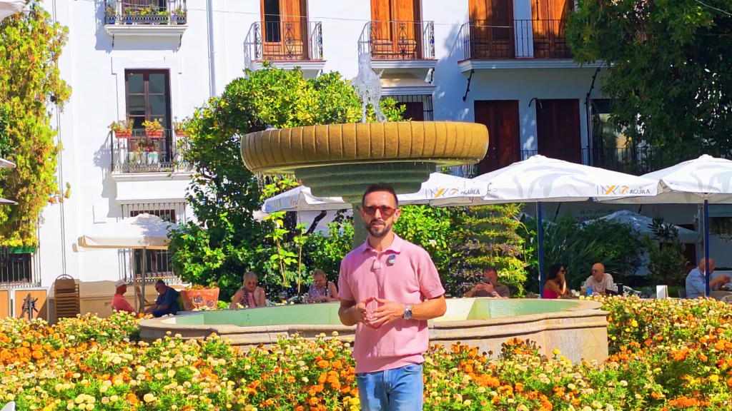 Izidor Isakov beside a fountain and colourful flowerbeds in an Estepona old town square.