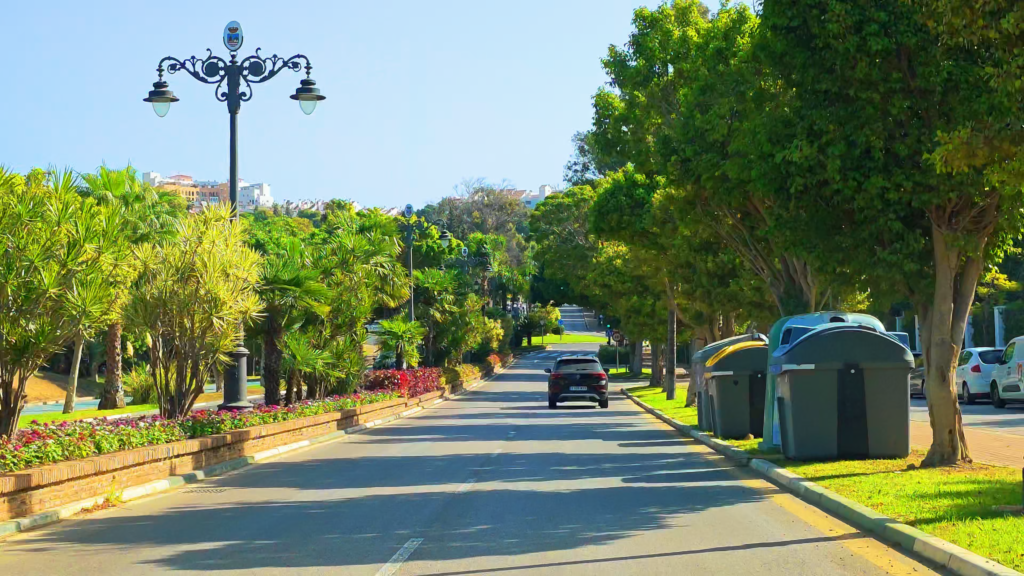 Tree-lined residential street in Estepona with planted verges and roadside recycling bins.