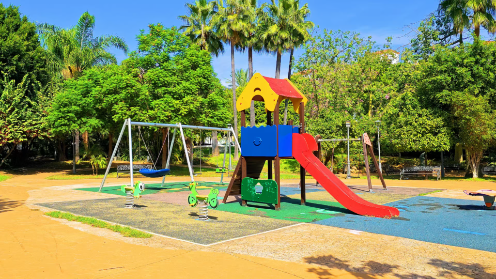 Colourful slide and swings in an Estepona playground surrounded by trees.